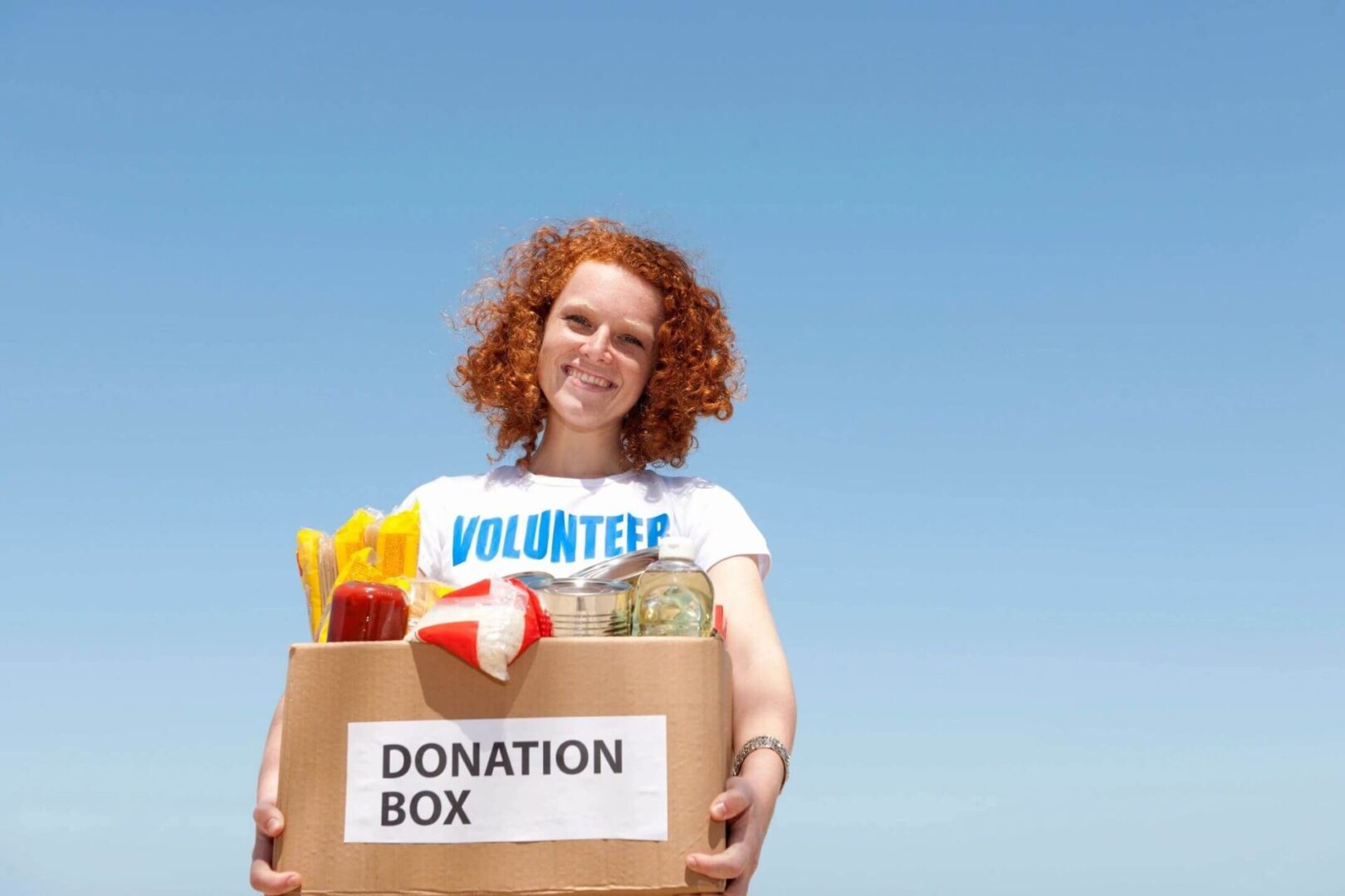 A woman holding a box of food in front of the sky.